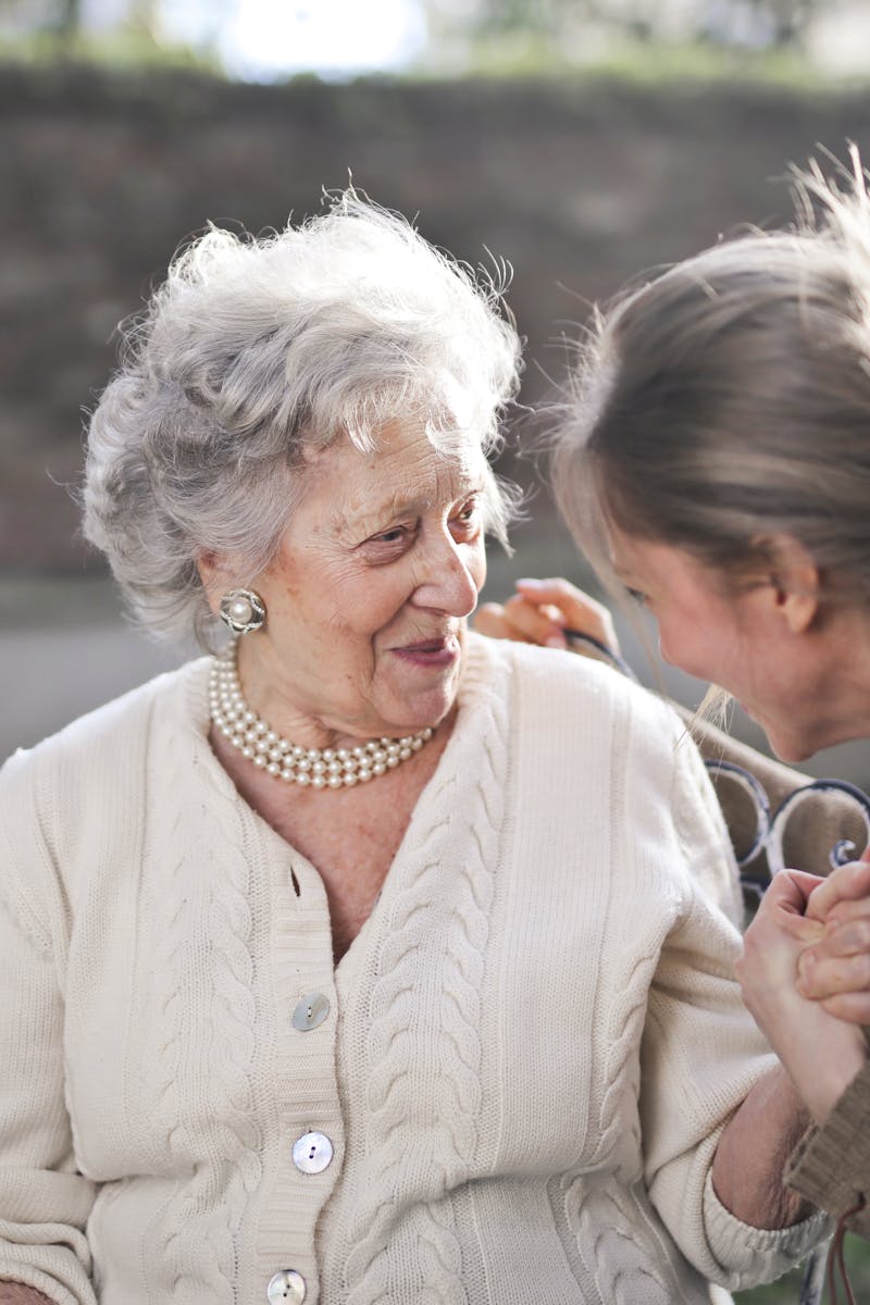 Joyful interaction between an elderly woman and her granddaughter in a sunny outdoor setting.